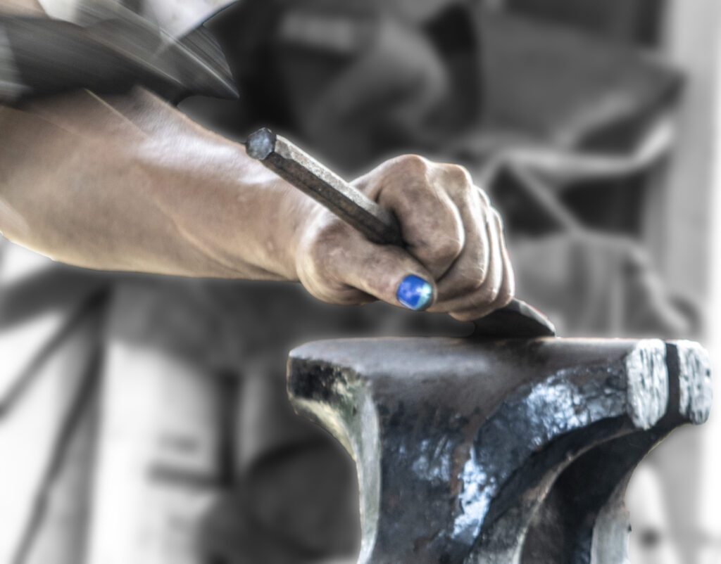 Hand of female blacksmith with blue nailpolish working on a vice.